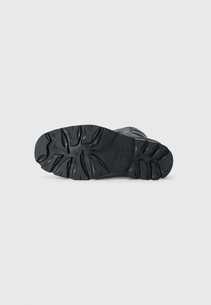 Semelle en caoutchouc noir d'une botte avec des crampons profonds et une surface texturée. Présentée en vue de dessus. Détails de marque et de taille gravés visibles.