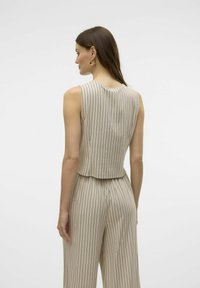 Top beige sin mangas con franjas verticales en azul marino, con un escote redondeado y una silueta ajustada, llevado con pantalones de cintura alta a juego.