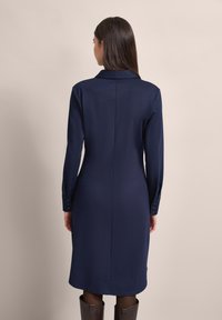 Marineblaue Langarmkleid mit kragenförmigem Ausschnitt, rückseitigem Nahtdetail und geknöpften Manschetten; glattes Material und knielanges Design.