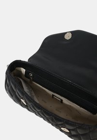 Borsa a tracolla nera trapuntata con finitura in pelle liscia, hardware in argento e tasca con zip interna contro una fodera in tessuto a fantasia.