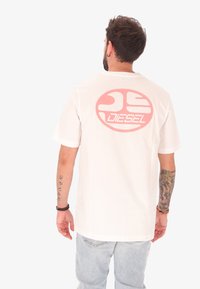 T-shirt en coton blanc présentant un grand logo circulaire rose avec le texte "DIESEL" au dos. Manches courtes et coupe décontractée.