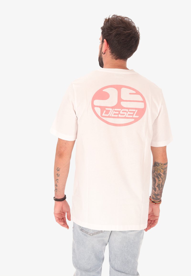 T-shirt en coton blanc présentant un grand logo circulaire rose avec le texte "DIESEL" au dos. Manches courtes et coupe décontractée.