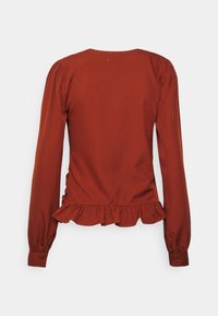 Blusa de manga longa em tecido cor ferrugem, com delicadas mangas bufantes, uma bainha em babados e punhos com botões. Textura suave, design simples.