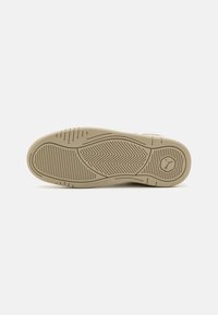 Beige színű sneaker talp, textúrált gumival és halszálkás mintázattal. Kerek logó a sarokban, sima felület kiegészítő barázdákkal.