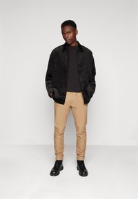 Camisa chaqueta de pana negra, camiseta negra, pantalones caqui y botas negras con cordones. Diseño sencillo con botones y sin patrones visibles.