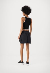 Fekete, rövidített tanktop fehér díszítéssel, sötét, pliszírozott szoknyával párosítva. A modellen fekete edzőcipő van, sima felülettel és egyszerű dizájnnal.