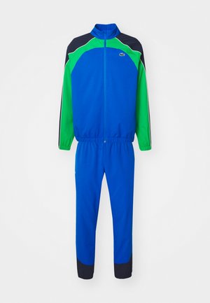 Fato de treino azul e verde com punhos e cintura elásticos, apresentando um colarinho alto, riscas laterais e um logótipo no peito. Acabamento em tecido durável.