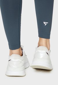 Helles graue Sportschuhe aus strukturiertem Material, mit weißen Akzenten und Polsterung. Begleitet von dunkelblauen, figurschmeichelnden Leggings mit Logodetails.