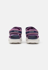 Lilla og marineblå sandaler med justerbare stropper, med en hvit såle og teksturert innersåle for pusteevne; merket med "GEOX."