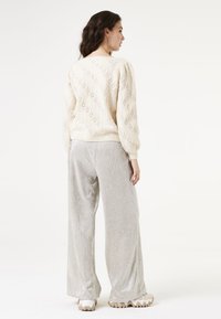 Lichtbeige gebreide trui met patroon en pofmouwen, gecombineerd met glanzende zilveren wijde broek en chunky witte sneakers.