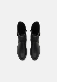 Par de botines de cuero negro con cremalleras laterales y hebillas decorativas, vistos desde arriba sobre un fondo claro y liso.