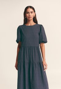 Vestito midi blu navy con maniche a palloncino, design a balze e dettagli sottili con motivo metallizzato in oro e rosso. Realizzato in tessuto strutturato.