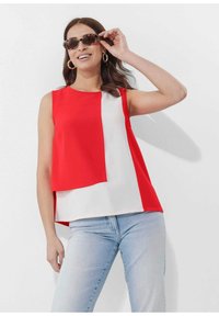 Rood en wit kleurblok mouwloos topje met een vloeiende uitstraling en zachte textuur. Model draagt donkere zonnebril en denim jeans.