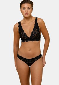 Bralette en dentelle noire avec un décolleté en V profond et des bords festonnés, associé à un string en dentelle assorti. Motif floral avec une texture transparente.