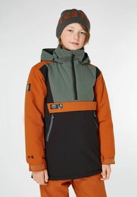 Farbblockierte Jacke mit einem grauen Oberteil, orangefarbenen und schwarzen Abschnitten. Verfügt über eine Reißverschlusstasche auf der Vorderseite und verstellbare Bündchen. Getragen mit einer grauen Mütze.