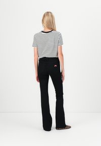 Black flared jeans with a high waist, paired with a striped short-sleeve shirt. Features a patch on the back pocket.