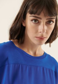 Blauw topje met korte mouwen, voorzien van een gladde textuur, een ronde halslijn en een subtiel kleurverloopontwerp.