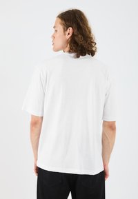 Hvid kortærmet T-shirt lavet af bomuld; afslappet pasform med rund hals og glat tekstur; vist fra ryggen mod en ensfarvet baggrund.
