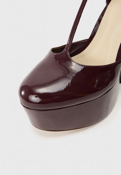 Bordowy lakierowany but na wysokim obcasie z okrągłym noskiem i paskiem T, wyposażony w grubą platformę dla większej wysokości.