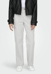 Onderlichaam van een persoon in witte gestreepte cargobroek, witte sneakers, zwart leren cropped jack en een witte top.