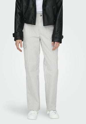 Onderlichaam van een persoon in witte gestreepte cargobroek, witte sneakers, zwart leren cropped jack en een witte top.