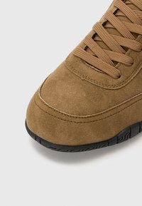 Braune Wildleder-Sneaker mit runder Spitze, strukturiertem Obermaterial und passenden Schnürsenkeln. Die schwarze Gummisohle verfügt über ein gemustertes Profil.
