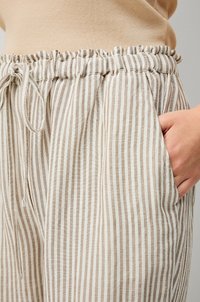 Pantaloni in lino a righe con cintura elastica, colori beige chiaro e bianco, caratterizzati da una vestibilità comoda e tasche laterali per funzionalità.