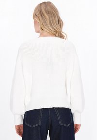 Hvid chunky strikket sweater med et cropped design, ribbede manchetter og detalje på ryggen. Sammen med mørkeblå højtaljede jeans.