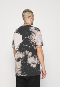 Camiseta de tie-dye en negro y beige con un corte oversize, mangas cortas y un cuello redondo, que presenta patrones irregulares y una textura de algodón suave.