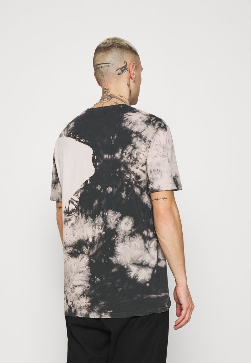 Camiseta de tie-dye en negro y beige con un corte oversize, mangas cortas y un cuello redondo, que presenta patrones irregulares y una textura de algodón suave.