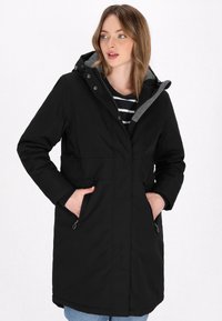 Cappotto lungo nero realizzato in tessuto impermeabile, con cappuccio foderato in grigio, tasche laterali e una lunghezza media.