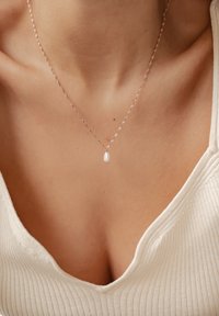 Halskette aus Roségold mit einem verdrehten Design und einem ovalen Perlenanhänger, der in der Mitte des Halses sitzt, vor einem hellen Stoff.