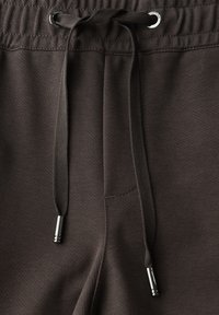 Nahaufnahme des dunkelbraunen Bunds von Jogginghosen mit gebundenem Kordelzug und metallenen Enden, die die Textur des Stoffes und die Nähdetails zeigen.
