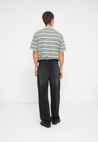Striped short-sleeve shirt in pale green and dark stripes paired with black wide-leg jeans. Smooth fabric with a relaxed fit and visible back pockets.