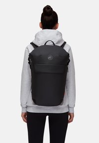 Sac à dos noir avec une finition lisse et mate, un dessus arrondi, une poche avant et un accent de logo ; porté par-dessus un sweat à capuche gris avec des cordons.