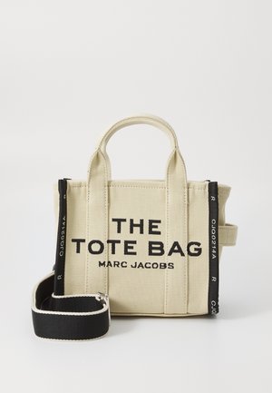 Geantă din pânză de culoare bej cu text negru "THE TOTE BAG MARC JACOBS." Dispune de mânere scurte și o curea neagră detașabilă.