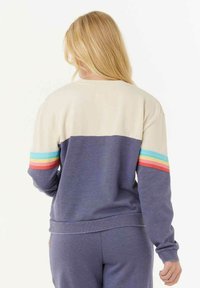 Sweatshirt mit einem oberen Panel in Creme und einem unteren Teil in Dunkelblau. Verfügt über bunte horizontale Streifen an den Ärmeln. Weicher Stoff, lässige Passform.