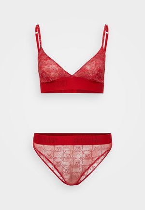 Bralette in pizzo rosso con spalline regolabili, caratterizzato da un motivo floreale e una fascia rossa uniforme. Slip in pizzo rosso abbinati con un design di orso sul tessuto.