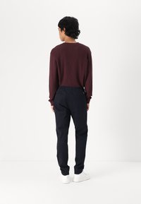 Burgunderfarget ribbestrikket langermet skjorte med rund hals, paret med marineblå bukser og hvite joggesko. Glatte teksturer og rene linjer.