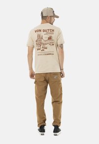 Camiseta de algodón beige con un diseño gráfico rojo del Monument Valley. Combinada con pantalones cargo color crema y zapatillas negras.