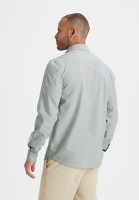 Lichtgrijs hemd met lange mouwen, een klassieke kraag, knopenmanchetten en een rechte zoom, gedragen met crèmekleurige broek. Zachte, gladde textuur.