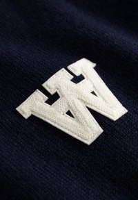 TâlĂŞ de tricot în nuanță de navală, cu un logo alb brodat mari, reprezentând litera "W". Textura este moale și ușor texturată, evidențiind detalii clare de coasere.