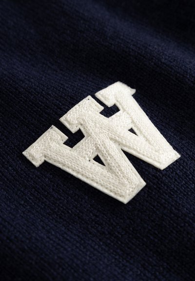 Navy knit fabric with a large white embroidered "W" logo. The texture is soft and slightly textured, showcasing clear stitching details.