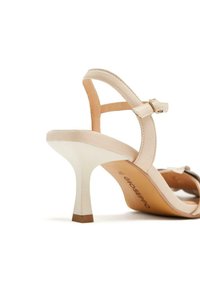 Sandal con tacco alto beige con finitura liscia, cinturino alla caviglia regolabile e tacco a stiletto sottile. Include un'occhiello decorativo a forma di fiocco.