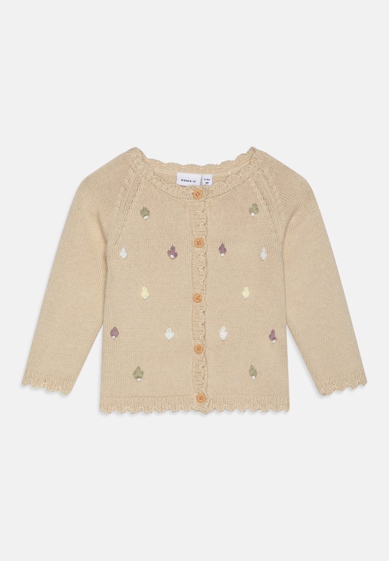 Bežani pleteni kardigan s valovitim izrezom, koji sadrži šarene vezenje motive i drvene dugmadi sprijeda. Dugi rukavi.