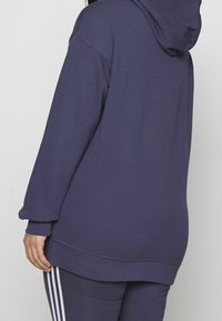 Marinblå oversized hoodie i bomullsblandning, lång ärm, ribbade muddar och nederkant, har en känguruficka och justerbar dragsko vid huvan.