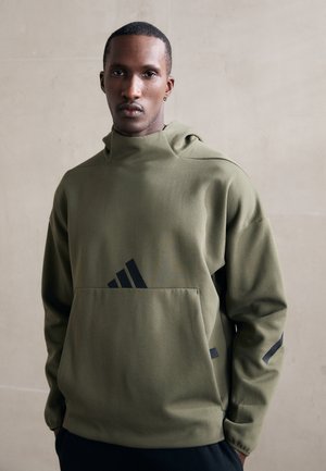 Sweatshirt à capuche vert olive avec une poche avant, arborant un logo noir et des rayures d'accent. Texture lisse et design moderne.