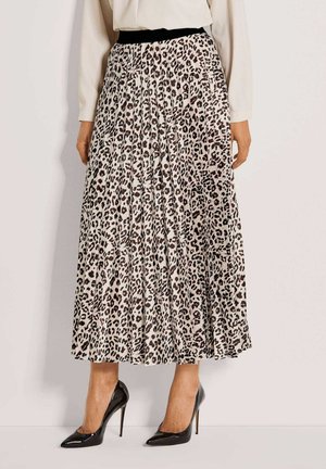 Frau trägt einen plissierten Leopardenprint-Midirock mit schwarzem Bund, schwarze High Heels und ein langärmeliges cremefarbenes Oberteil.
