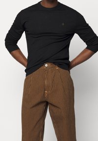 Camisa negra de manga larga con puños acanalados, combinada con pantalones marrones de rayas que tienen un cierre de botón y corte recto.