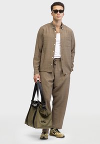 Light brown textured shirt with white buttons, matching pants, black sunglasses, and an olive green bag with a black strap and logo.